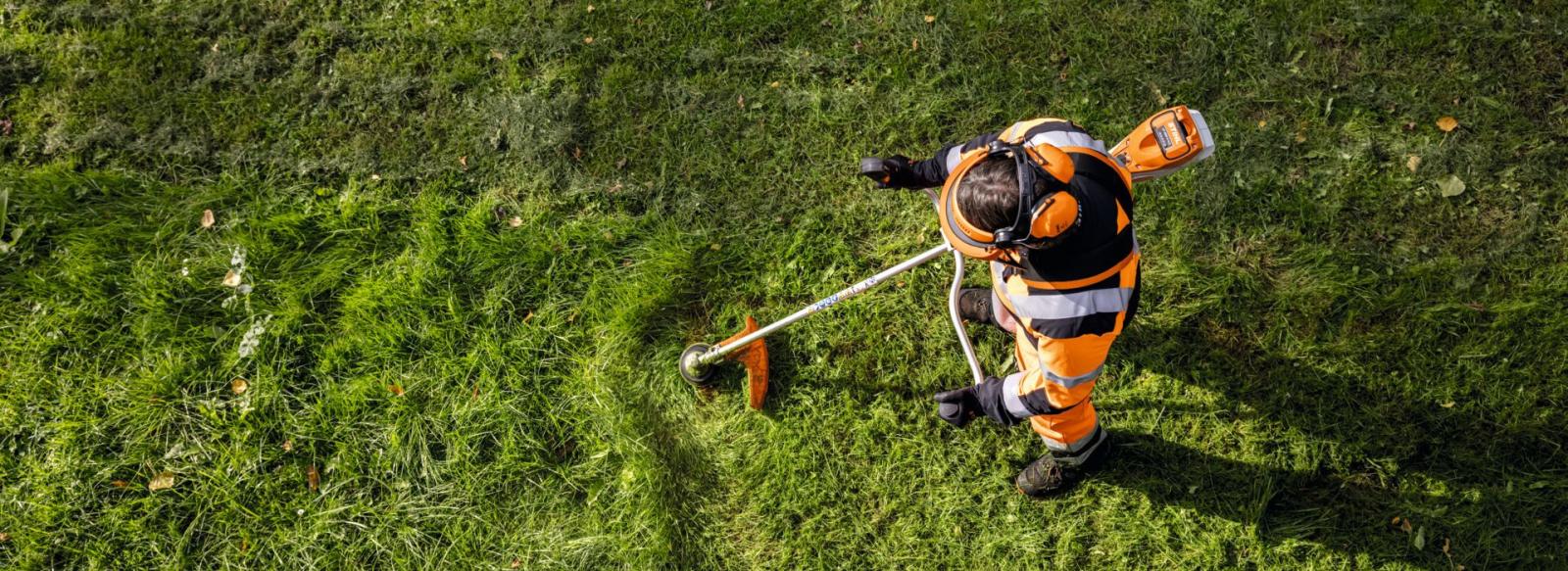 Vue de dessus, un homme qui débroussaille un champs avec une débroussailleuse à batterie Stihl